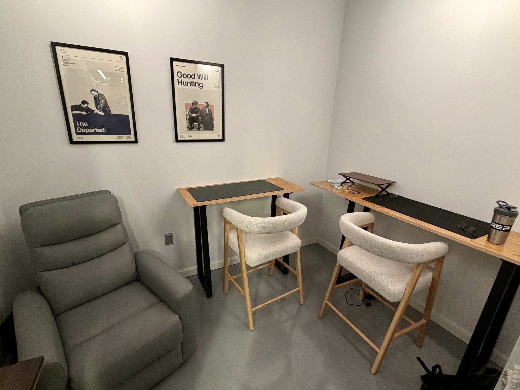 A co-working room with two standing desks, stools and a recliner